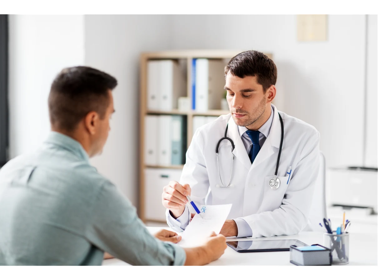 A doctor in a white coat explains a document to a seated patient in an office setting.